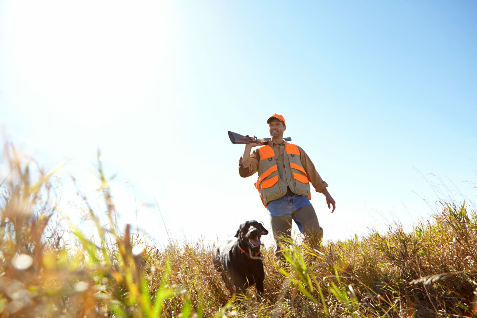 A hunter holding his shotgun while standing outdoors with his hunting dog